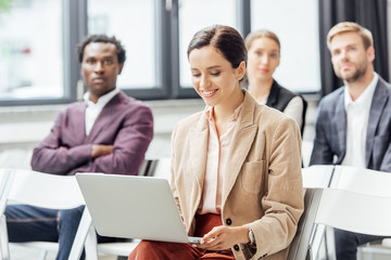 selective focus of attractive woman in formal wear holding laptop during conference