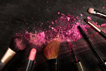 Make-up brushes and lipstick with crushed cosmetics, overhead shot on a black background with copy...
