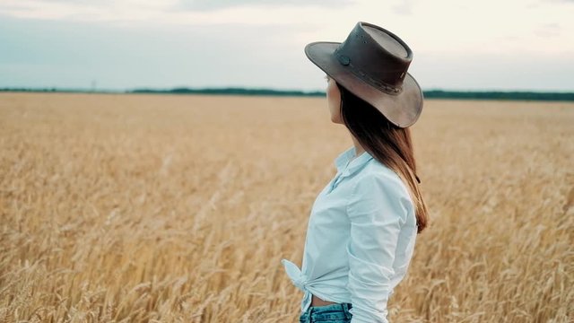 Beautiful girl in a shorts and hat walking through a wheat field at sunset. Freedom concept. Wheat field in sunset