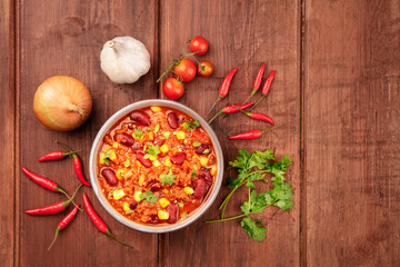Chili con carne, shot from above on a dark rustic wooden background with ingredients and a place for text