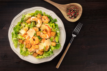 Shrimp Caesar salad with Parmesan cheese, croutons and lettuce, shot from the top on a dark rustic wooden background with copy space
