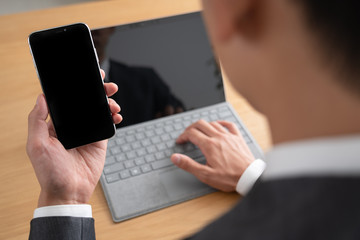 スマートフォンをみながらパソコンを使うビジネスマン