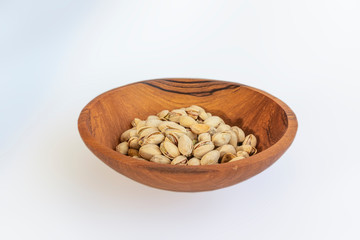 Pistachios in wooden bol as appertiser with drinks against a white background