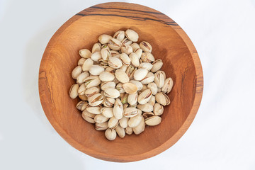 Pistachios in wooden bol as appertiser with drinks against a white background