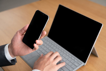 スマートフォンをみながらパソコンを使うビジネスマン