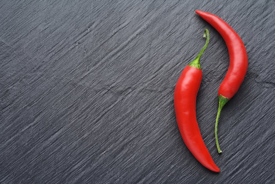 Red chili peppers on dark black slate background with copy space. Top View