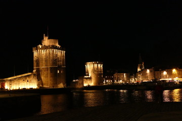 Fototapeta na wymiar La Rochelle old port (Vieux Port) lit up at night, showing Tour Saint Nicholas (on the left) and Tour de la Chaine (on the right) guarding the entrance to the harbour