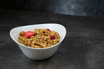 Muesli with srawberry and cranberry in white bowl on grey background.