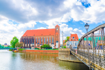 Fototapeta premium Roman Catholic parish Saint Mary church NMP on the Sand island Wyspa Piasek and Mill Mlynski bridge over Oder Odra river in old historical city centre of Wroclaw, Poland