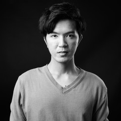 Young handsome Asian man against black background
