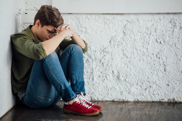 sad teenager in jeans holding smartphone and sitting on floor