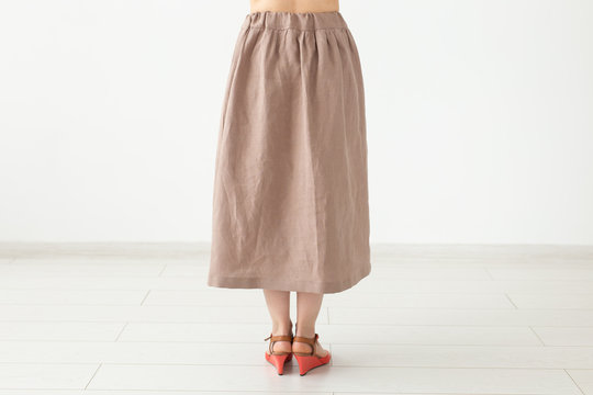 Young unidentified girl in a brown long skirt and shoes stands neara white wall. The concept of feminine design products