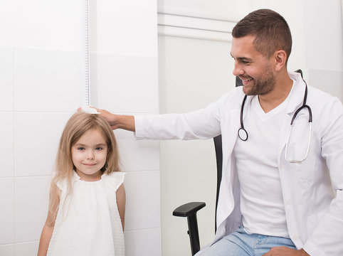 The doctor measures the growth of a little girl. Pediatrician and little patient