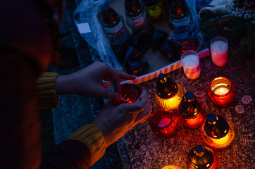 Woman light on red and yellow candles in the dark - to put them on a tombstone - all souls day preparing in the cemetery