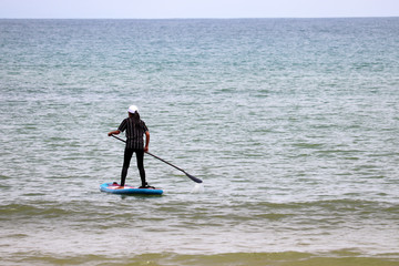 Fototapeta na wymiar Sup surfing, girl with paddle standing on a board in open sea. Standup paddleboarding in SouthEast Asia