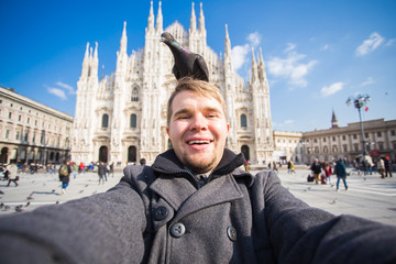 Winter travel, vacations and birds concept - Young funny man taking selfie with pigeons near Milan Cathedral Duomo di Milano, Italy.