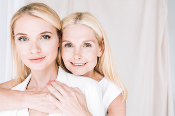 happy blonde mother and daughter in total white outfits hugging each other