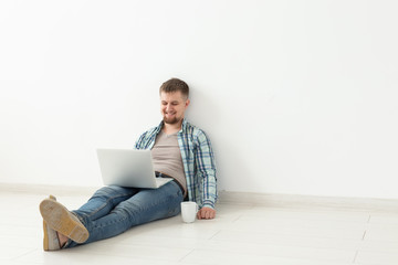 Positive young man in casual clothes and glasses surfing the Internet using Wi-Fi and a laptop in search of rental housing. Housewarming and apartment search concept, copy space