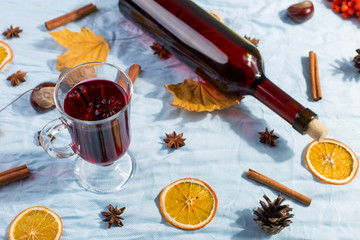 A cup of mulled wine with spices, bottle, dry leaves and oranges on table. Autumn mood, method to...