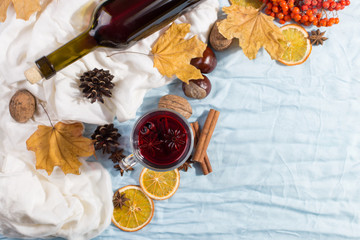 A cup of mulled wine with spices, bottle, dry leaves and oranges on table. Autumn mood, method to keep warm in the cold, copy space, morning light.