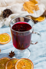 A cup of mulled wine with spices, dry leaves and oranges on the table. Autumn mood, a method to keep warm in the cold, copy space, morning light.