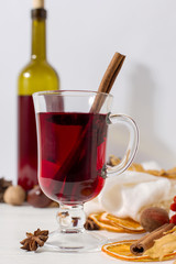 A cup of mulled wine with spices, bottle, scarf, spices, dry leaves and oranges on the table. Autumn mood, method to keep warm in cold, copy space.