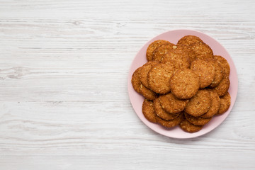 Cereal cookies on a pink plate on a white wooden background, top view. Flat lay, overhead, from above. Copy space.