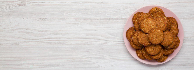Cereal cookies on a pink plate on a white wooden background, top view. Flat lay, overhead, from above. Space for text.