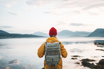 Alone traveler wearing yellow raincoat and backpack looking at fantastic fjord and mountain...