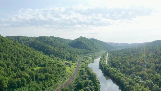 Flying on a river valley with a railway and a freeway along the river. Beautiful landscape of mountain forest on a sunny morning.