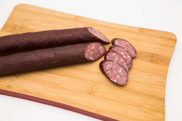 Deer home sausages with thin slices on a wooden board. Wild meat delicacies for gourmets  on white background.