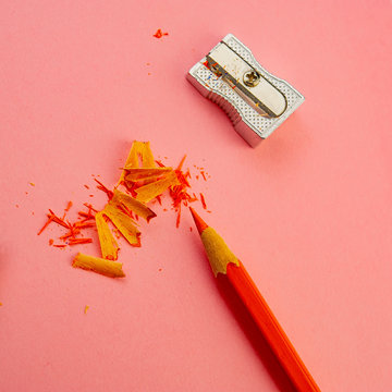 fine cut shavings with an orange pencil and a sharpener lie on a pink background.