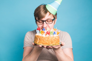 Crazy funny young man in glasses and paper congratulatory hats holding cakes happy birthday standing on a blue background.