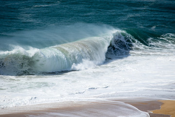 Beautiful crushing wave of Atlantic ocean, captured during the walk along the sandy beach in Nazare, Portugal