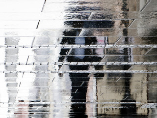 Blurry reflection shadow silhouette of  a man in black suit walking under umbrella on a rainy day