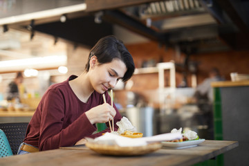 Portrait of smiling young woman enjoying delicious food while sitting at table in Asian cafe or restaurant, copy space