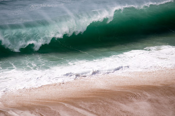 Beautiful crushing wave of Atlantic ocean, captured during the walk along the sandy beach in Nazare, Portugal