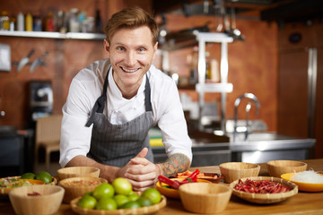 Portrait of contemporary chef smiling at camera while posing with spices in restaurant kitchen, copy space