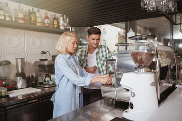 Two baristas working at the coffee shop. Handsome male barista teaching new employee using coffee machine. Cafe, profession, employment concept