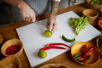 Closeup of unrecognizable chef cutting limes and hot pepper while cooking spicy Asian food in restaurant kitchen, copy space