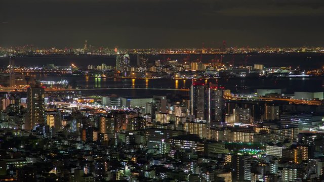 Timelapse zoom out Kobe night coastal metropolis seaport panorama in Japanese city harbour surrounded by highways among skyscrapers and highrise buildings with bright colorful illumination