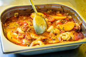 Close up of large portion of seafood cooked with vegetables in tomato sauce, available for sale at a street food market, selective focus