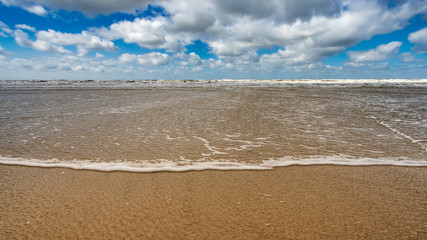 Flachwasser Wellen am Strand mit Weitsicht und Wolken