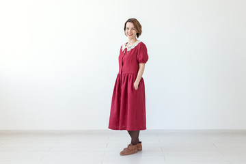 Positive beautiful young smiling woman posing on white background red modest dress. Concept of a stylish young girl.