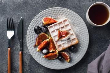 Fototapeta na wymiar Traditional Belgian waffles with powdered sugar grapes and figs. Cozy homemade Breakfast. Gray concrete background. Copy space.
