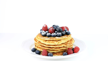 Pila di pancakes con miele, mirtilli neri e lamponi rossi spolverati con zucchero a velo su sfondo bianco