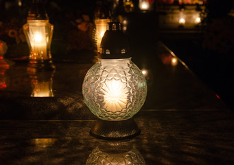 Candle in an elegant lantern on a marble tombstone - in the background more lantern - all souls night decoration in the dark - european christian cemetery