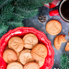 Cookies on a red plate with coffee in a red mug on a table with branches, top view, selective focus