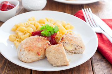 Homemade turkey cutlets with cheese filling on a white plate on a wooden table, horizontal