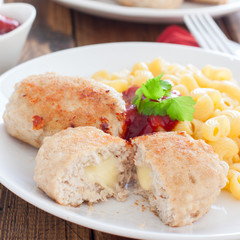 Homemade turkey cutlets with cheese filling on a white plate on a wooden table, square